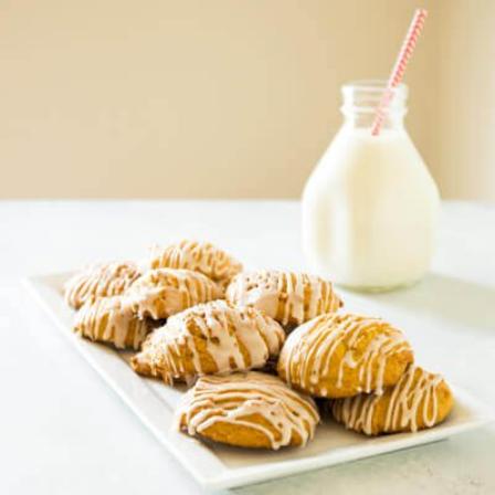Image of a white plate with about ten, round, tan cookies with stripes of white glazed on top of them. Next to this plate is a small glass bottle of milk with a red straw in it.
